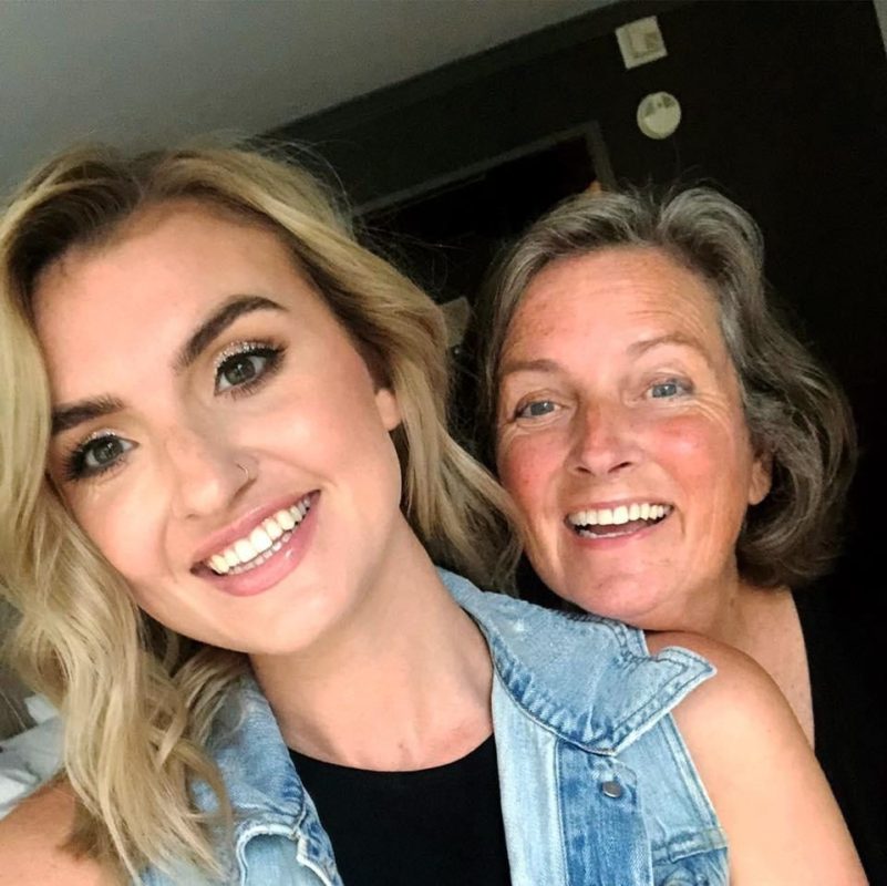 A picture of a woman with grey/brunette hair with her daughter who has blonde hair. They both are smiling.