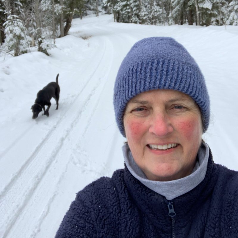 A picture of a smiling woman in a blue hat walking outside with her dog.