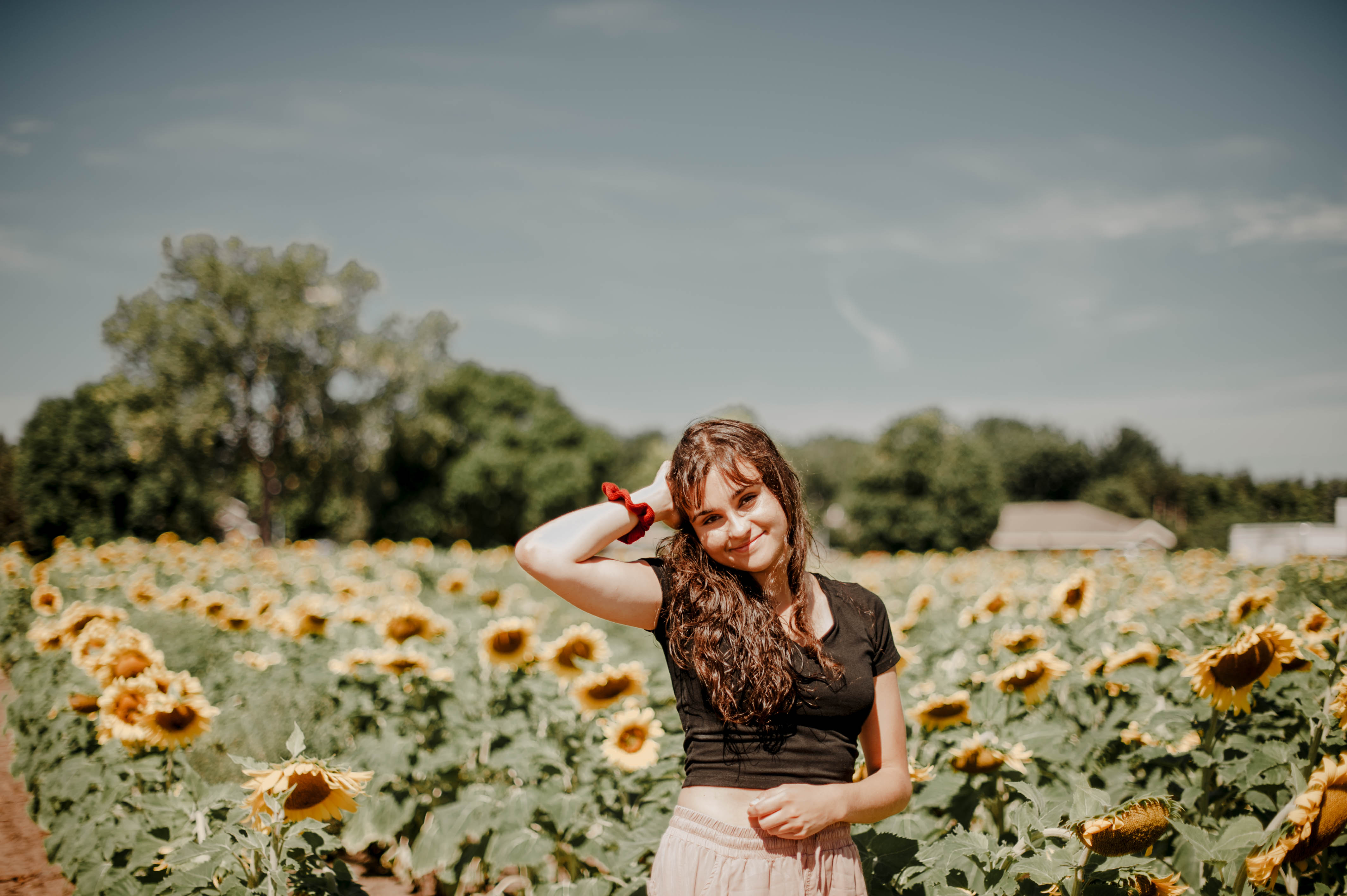 A picture of a woman with long curly brown hair smiling in a sunflower field.