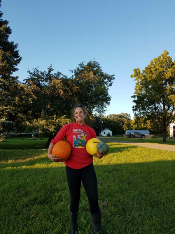 A picture of a woman with her hair pulled back outside holding a variety of sports balls.