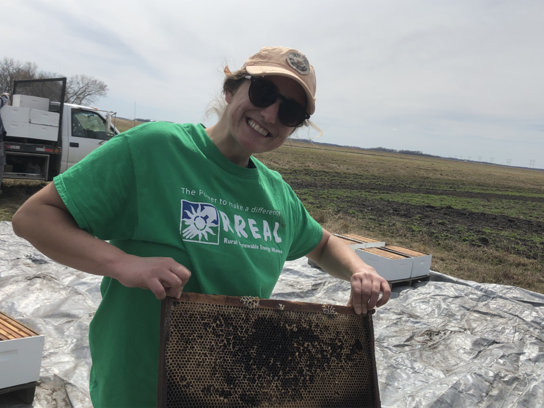 A picture of a woman wearing a hat and sunglasses wearing a green t-shirt. She is doing work in the field.