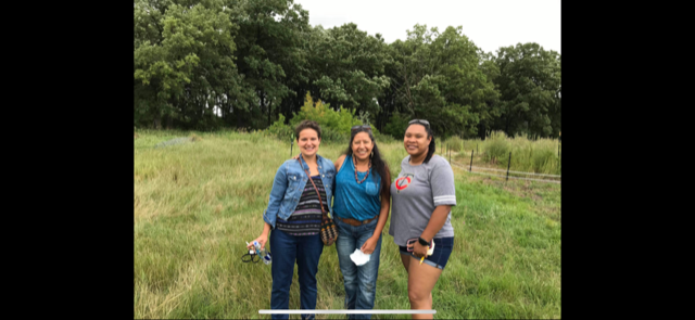 A picture of three women posing together in a green field.