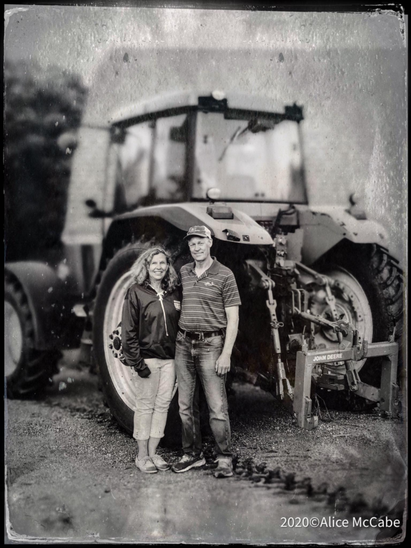 A black and white picture of a woman and her husband in front of a tractor.