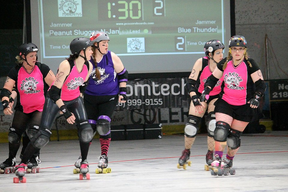 A picture of women playing dirty roller. They are all wearing uniforms, four in pink uniforms and one in a purple uniform.