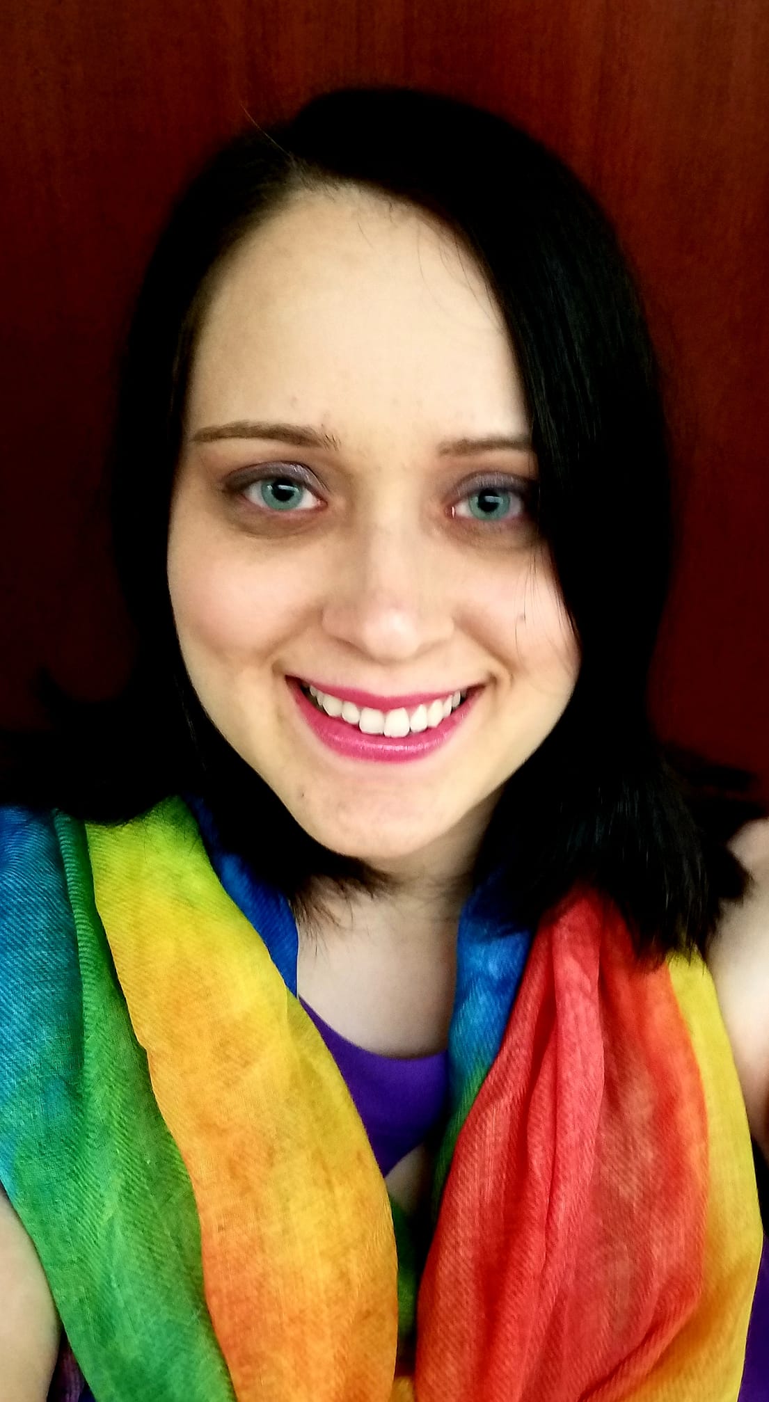 A picture of a woman with short dark hair wearing a rainbow scarf smiling.