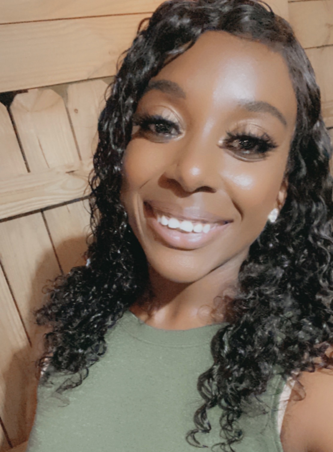 A picture of a black woman with dark curly hair wearing a green shirt smiling.