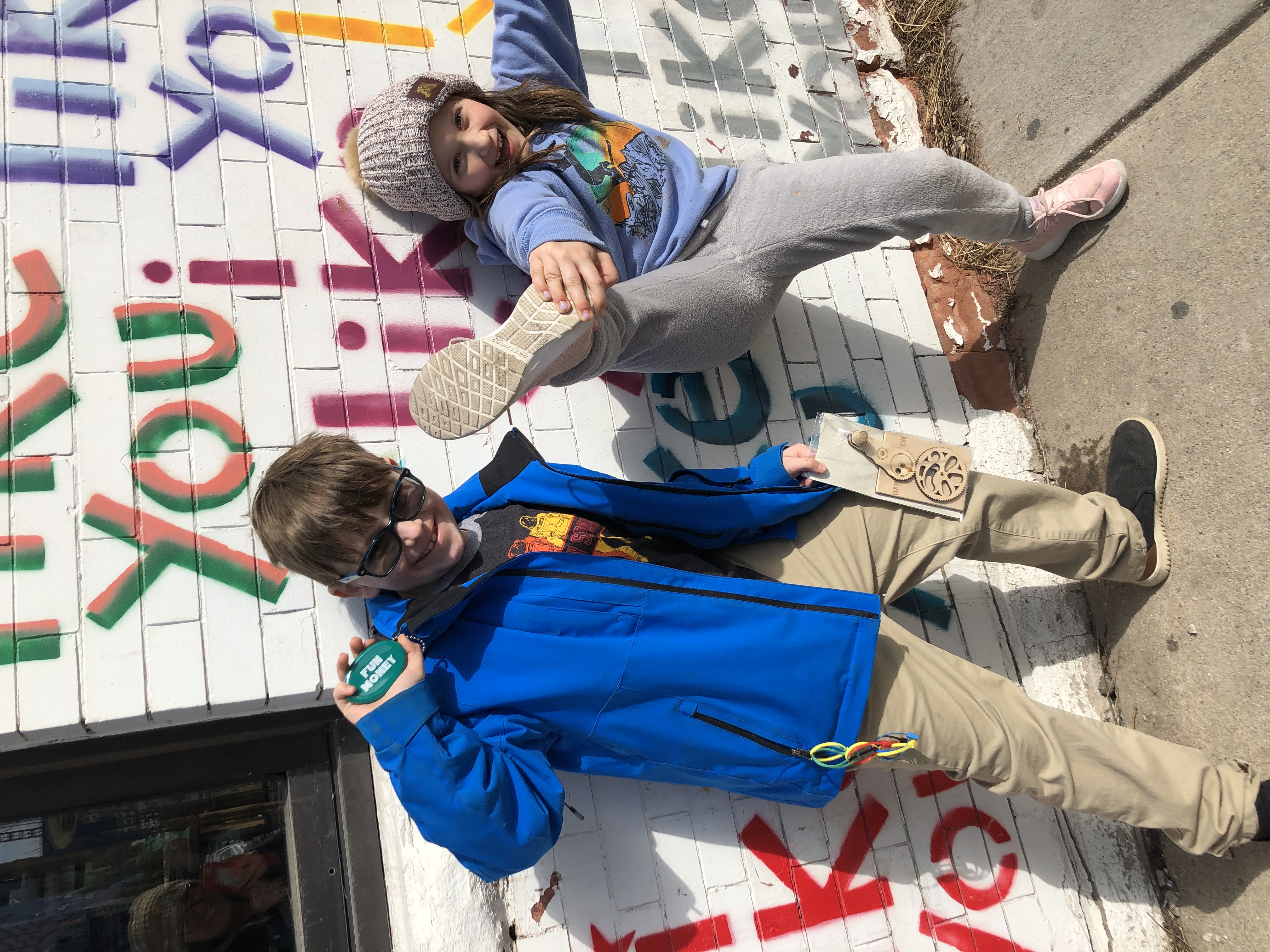A picture of two children together in front of a painted brick mural.