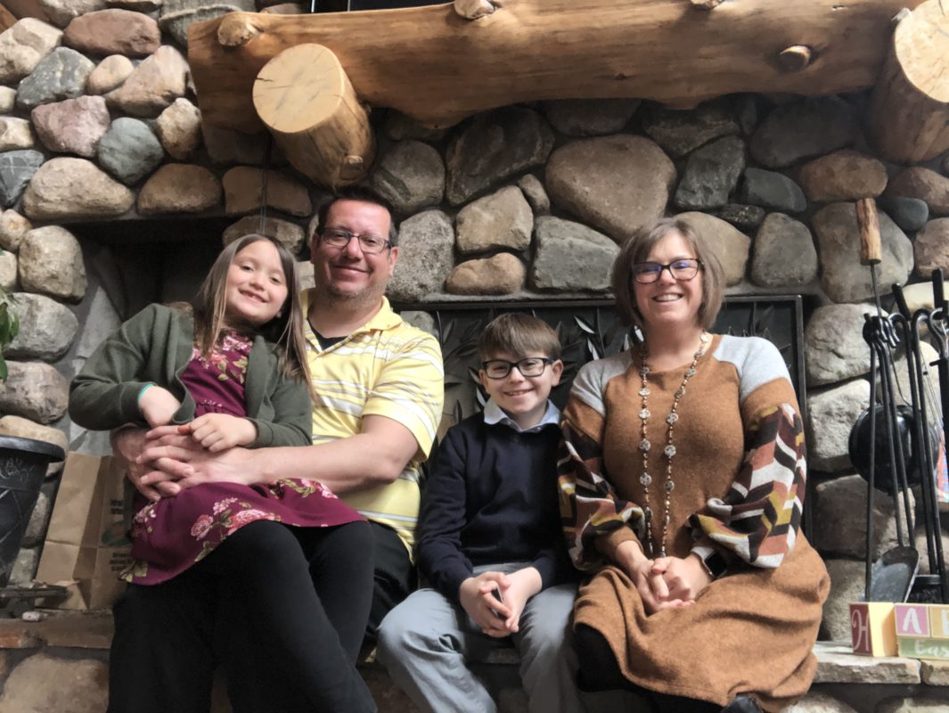 A picture of a a family in front of a stone fireplace.