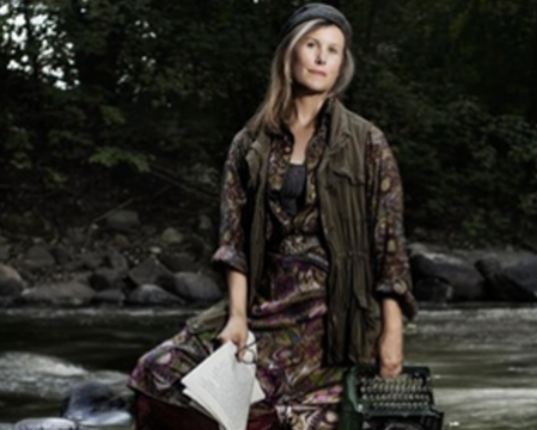 A picture of a woman wearing patterned clothing standing in a river holding papers, glasses, and a typewriter.