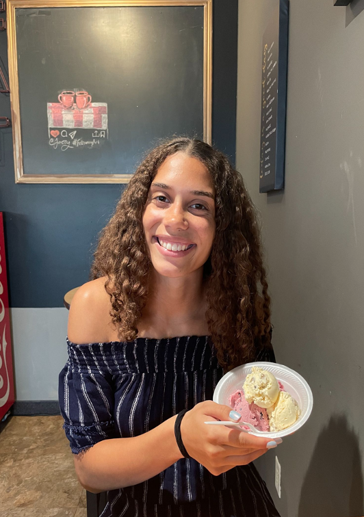 A picture of a woman with long, curly brunette hair smiling and holding ice cream.