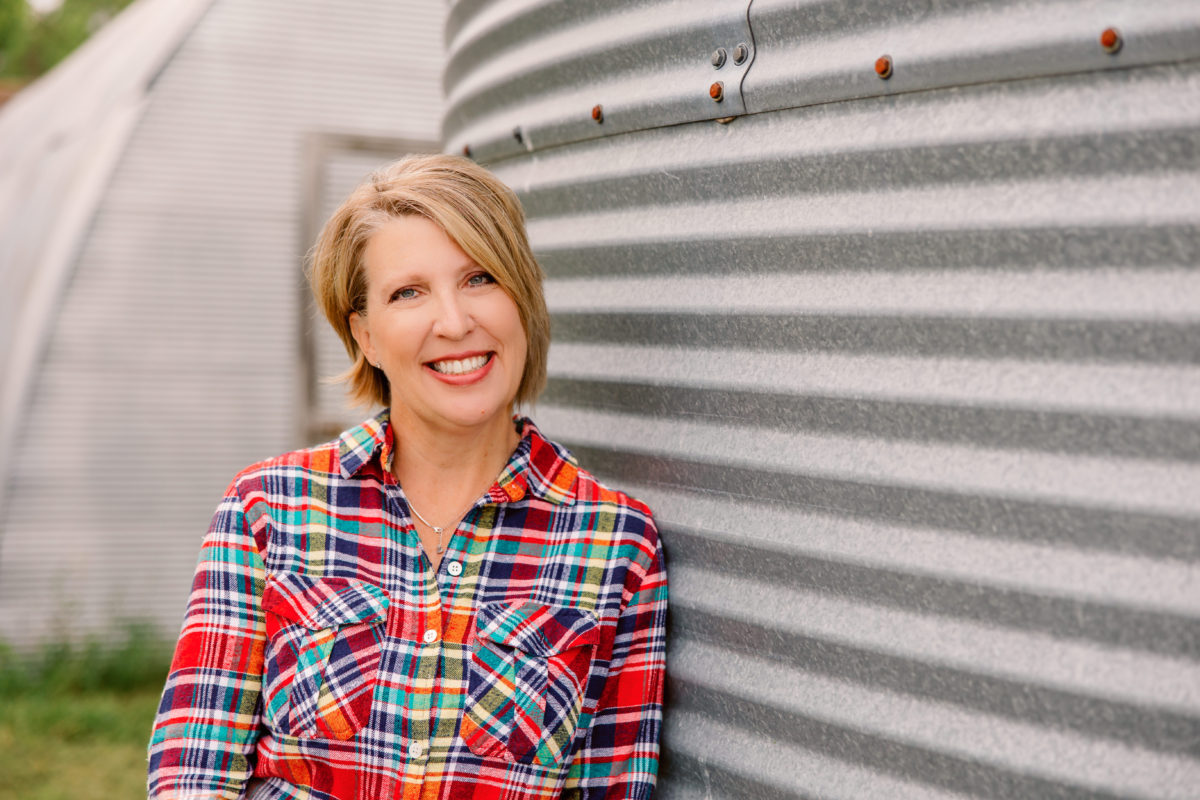 Smiling blonde woman wearing a plaid shirt leaning against a grain bin