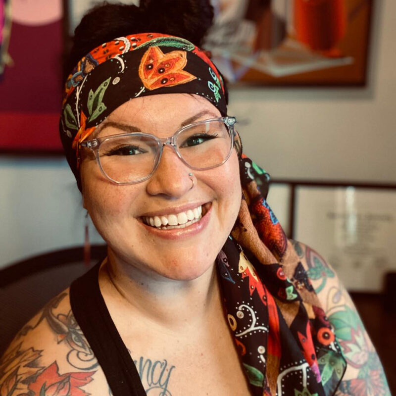 Fawn smiles at the camera. She is wearing glasses and a colorful head scarf.