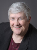 A picture of a woman with short, grey hair smiling. She is wearing a black jacket and a maroon shirt.